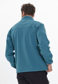 Blå softshell-jacka med hög krage; har sömdetaljer och en mjuk textur; bärs med svarta byxor som ger en avslappnad passform.