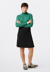 Groene gebreide coltrui, zwarte rok tot de knie, en multicolore sneakers met strepen. Soepele textuur van het breiwerk en de stof van de rok.