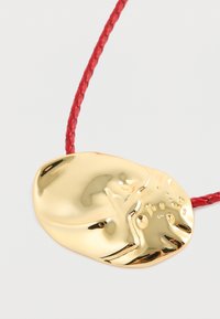Czerwona, pleciona koralikowa naszyjnik z błyszczącym, nieregularnym złotym wisiorkiem posiadającym gładką powierzchnię i subtelnie wytłaczane kropki.