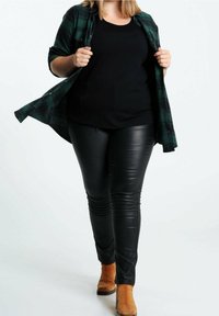 Czarny top, zielona flanelowa koszula w kratę, czarne spodnie z ekologicznej skóry oraz beżowe botki za kostkę. Strój charakteryzuje się warstwową fakturą i dopasowanym krojem.