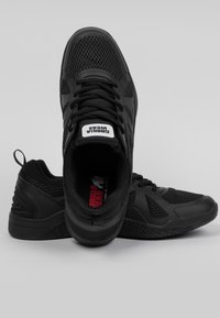 Baskets de sport noires avec une tige en maille pour la respirabilité, semelle extérieure en caoutchouc texturé et logo emblématique sur la languette.
