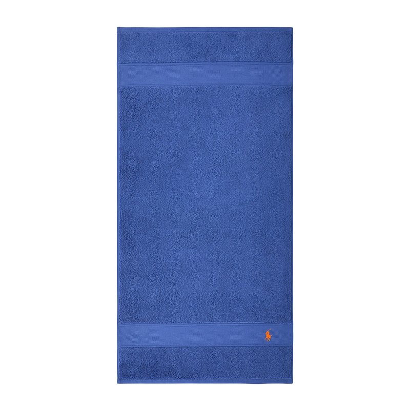 Μπλε βαμβακερή πετσέτα μπάνιου με υφή στην επιφάνεια, μονόχρωμη και κεντημένο πορτοκαλί λογότυπο κοντά στο κάτω μέρος.