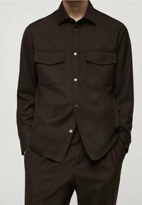 Chemise marron à boutons fabriquée en tissu texturé, dotée de deux poches poitrine, d'un col classique et d'une fermeture à boutons à l'avant.