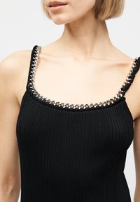 Γυναίκα που φοράει μαύρο ριμπ τιραντάκι με ασημένια αλυσίδα που είναι πλεγμένη γύρω από το λαιμό και τους ιμάντες.