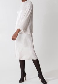 Lys elfenben farvet bluse og nederdel sæt, med lange ærmer, høj halsudskæring og et svævende design, parret med sorte ankelremssandaler.