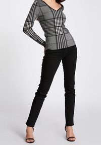 Jeans skinny negros combinados con una blusa ajustada de estampado gris y negro que presenta un escote en V y mangas largas. La blusa tiene un diseño texturizado.