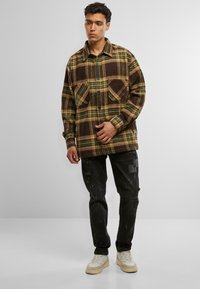 Brun og grønternet skjortejakke, knappet med to brystlommer; båret med sorte slidte jeans og beige sneakers.