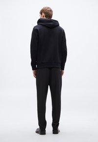 Črna kapucar s kapuco in ujemajoče se hlače, narejeni iz mehke tkanine, z rebrastimi manšetami in robom. Enostavna zasnova, brez vidnih vzorcev ali logotipov.