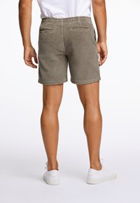 Pantalones cortos de pana en verde olivo, con una cintura elástica, dobladillos enrollados y dos bolsillos traseros. Llevados con zapatillas blancas.