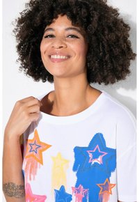Hvid t-shirt med korte ærmer, der har et farverigt stjernedesign i pink, orange, gul og blå. Den har en afslappet pasform og rund halsudskæring.