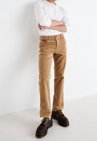 Kapsáčové kalhoty z kordu v béžové barvě se střihem rovného nohavice. Disponují bočními kapsami a zapínáním na knoflík. Kombinováno s tmavými šněrovacími botami a bílou košilí.
