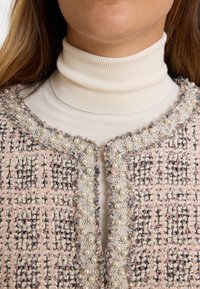 Roze en crèmekleurige tweedjack met parelaccenten, een textuurpatroon en een ronde halslijn. Voorzien van een haaksluiting aan de voorkant.