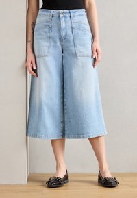 Lyseblå denim culotter med vide ben, høy midje, frontlommer og rå kant. Kombinert med svarte flate sko.