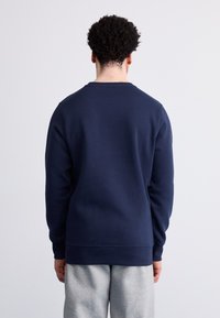 Sudadera azul marino con cuello redondo, mangas largas, puños y dobladillo acanalados, hecha de tela suave. Llevada con pantalones grises claros.