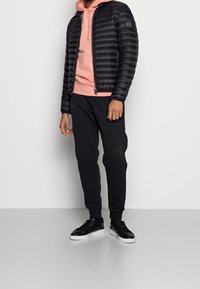 Svart puffjacka med en åtsittande design, kombinerad med en ljusrosa hoodie och svarta joggers. Svarta sneakers fulländar outfiten.