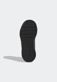 Černá gumová podrážka boty s texturovaným vzorem kruhových úchopů a horizontálních linií, na které je výrazně umístěno logo Adidas.