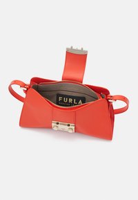 Sac à main en cuir rouge avec un design de nœud structuré, un fermoir en métal doré et un intérieur zippé révélant une doublure marron avec le logo de la marque.