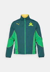 Puma-jakke i teal og grønn, med glidelås foran, høy krage, kontrasterende gule detaljer og logo på brystet. Vindjakke stil.