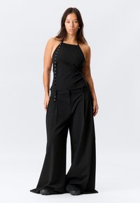 Haut noir à col licou avec détails de boutons latéraux, associé à un pantalon noir à jambes larges, tous deux en tissu lisse. Design simple et monochrome.