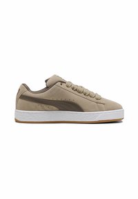 Beige suede sneakers with a brown leather logo, flat laces, and white rubber sole. Features perforated side detailing and textured outsole.