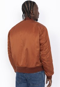 Bruine satijnen bomberjack met ribgebreide kraag en boorden, met een gladde textuur en gestikte details, gecombineerd met blauwe denim broek.