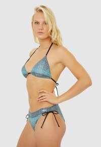 Ensemble de bikini avec un motif géométrique bleu, haut triangulaire avec des bretelles noires, et bas assortis avec des nœuds sur les côtés et un tissu texturé.