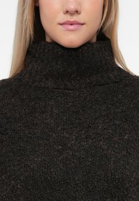 Dunkelbrauner Pullover mit hohem Kragen aus strukturierter, flauschiger Material, mit einem gerippten Kragen und ohne sichtbare Muster oder Hardware-Details.