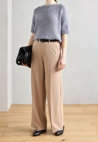 Hellgrauer, gestrickter Pullover mit kurzen Ärmeln, beige, weit geschnittene Hose, schwarzer Gürtel, strukturiertes schwarzes Handtasche in der Hand gehalten und schwarz, flachabsatz Schuhe.