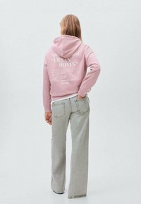 Ljusrosa huvtröja med grafisk text fram, ihop med ljusgrå utsvängda jeans. Huvdesign med känguruficka och ribbade muddar.
