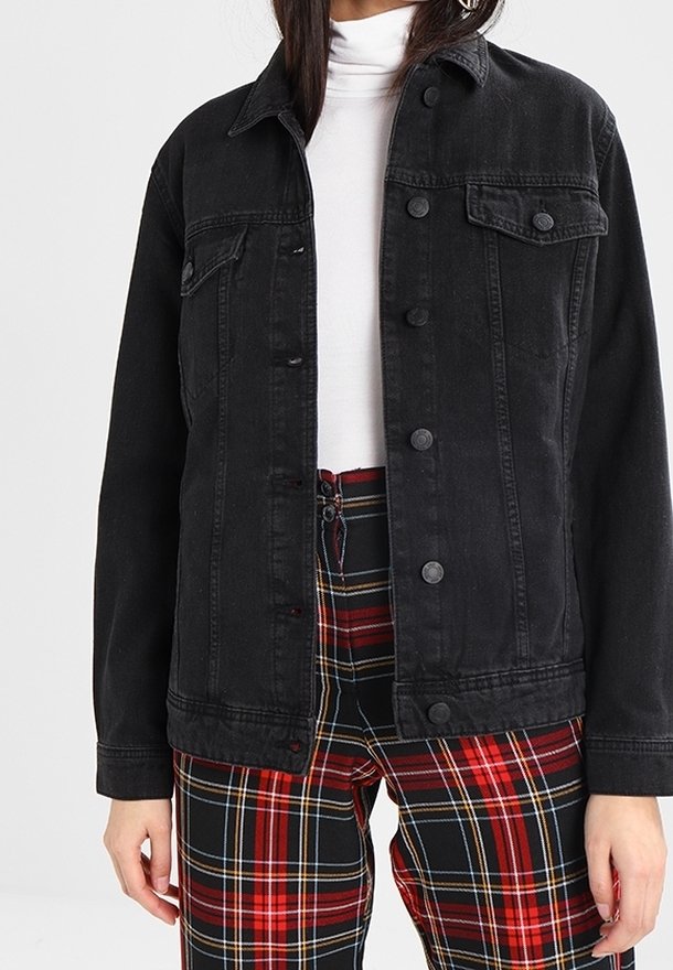 Giacca di denim nera con chiusura a bottoni, due tasche sul petto e una vestibilità rilassata, abbinata a pantaloni a quadri rossi e neri.