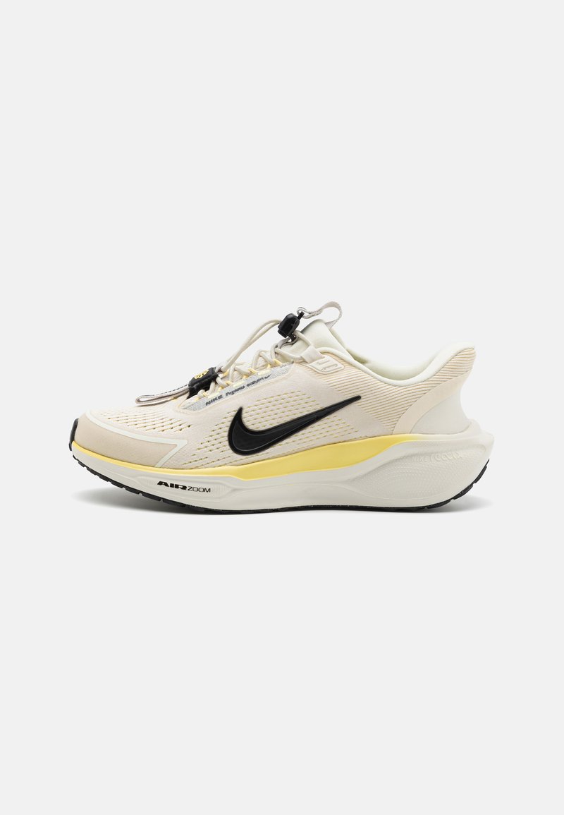 Bež sportski tenisica s crnim swoosh logotipom, žutim naglascima, prozračnim mrežastim gornjim dijelom, okruglim vrhom i teksturiranim gumiranim potplatom.