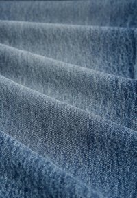 Tela de denim en azul claro, con una superficie texturizada que presenta patrones de sarga diagonal, mostrando suaves pliegues y arrugas.