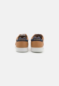 Sneaker in pelle marrone con suole in gomma bianche, che presentano un colletto imbottito e accenti blu sul tallone, insieme a dettagli del logo.
