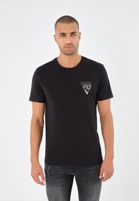 T-shirt en coton noir avec un col rond, des manches courtes et un design graphique triangulaire blanc sur la poitrine gauche. Coupe slim.