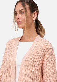 Gebreide cardigan in zachtroze, met een V-hals, open voorkant en een gevarieerd patroon. Inclusief een witte top eronder.