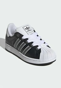Black leather sneaker with white rubber shell toe, three white stripes, and white laces. Features a textured upper and padded collar.