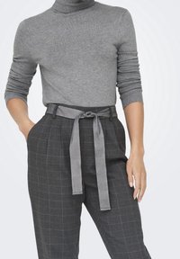 Pull à col roulé gris associé à un pantalon gris à carreaux taille haute, avec une ceinture assortie nouée à la taille. Texture lisse.