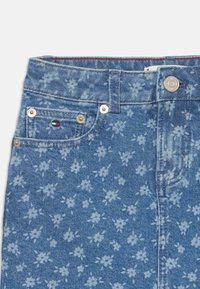 Jeans i denim med et lyst blått blomsterdesign, klassisk fem-lommers utforming med sølvfarget detaljer og et midjebånd med røde aksenter.