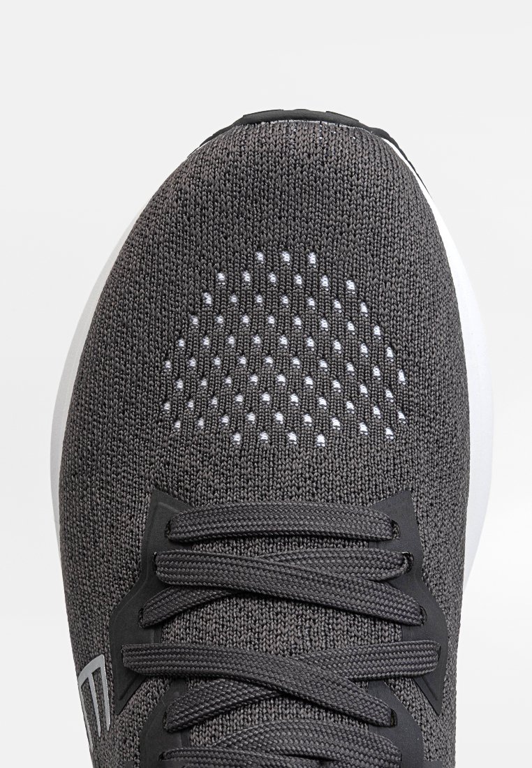 Grau sportlicher Schuh mit einem strukturierten Strick-Obermaterial, das einen gemusterten Mesh-Bereich im Zehenbereich und schwarze Schnürsenkel auf einer weißen Sohle aufweist.