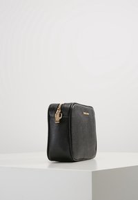 Borsa a tracolla in pelle nera con finitura testurizzata, hardware dorato e chiusura con zip. Forma rettangolare con angoli arrotondati.