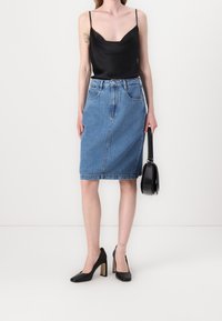 Camiseta de satén negra con tirantes finos, falda lápiz de mezclilla azul, zapatos de tacón altos negros y un pequeño bolso negro.
