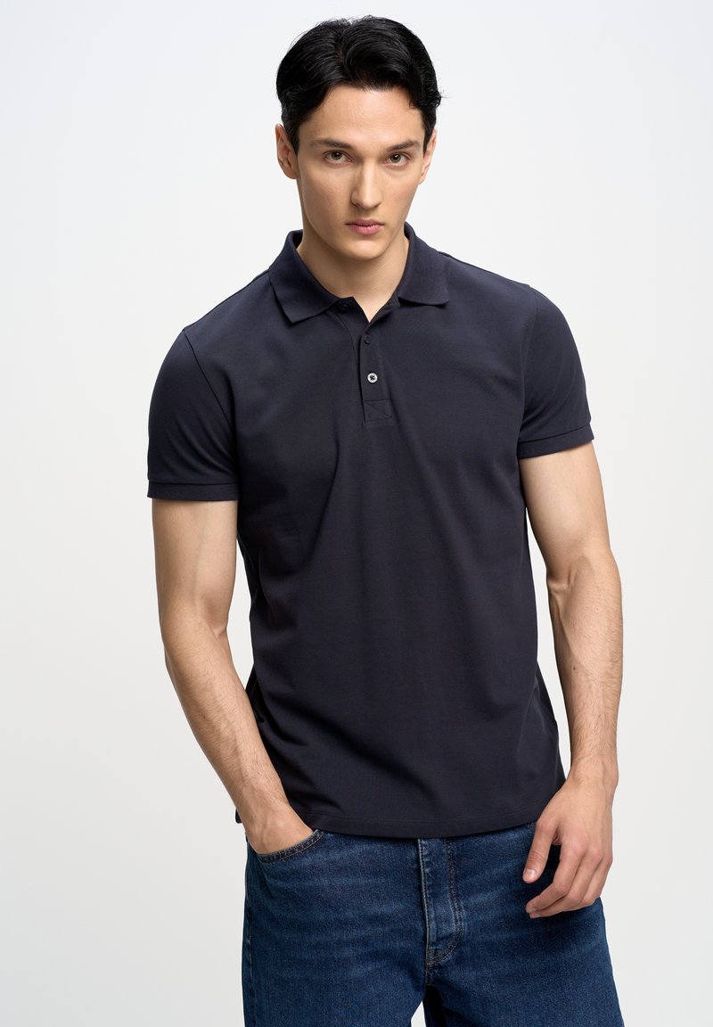 Jūros laivyno polo marškiniai, pagaminti iš lygaus audinio, su apykakle, trimis mygtukais, trumpomis rankovėmis ir tekstūruotu paviršiumi. Dėvimi su džinsais.