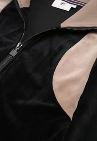 Musta ja beige vetoketjullinen takki, jossa on pehmeä, samettinen pinta, ja joka sisältää kontrastoivan beigen paneelin sekä hopeisen vetoketjun yksityiskohdan.