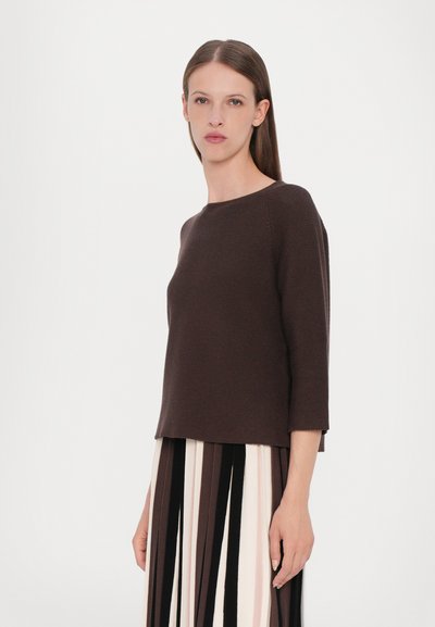 Pull en laine marron tricoté avec des manches trois quarts, présentant une texture côtelée et une coupe décontractée, associé à une jupe multicolore à rayures.