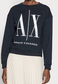 Mörkblå sweatshirt i bomull med en stor vit "A/X"-logotyp och texten "ARMANI EXCHANGE", med ett elastiskt band vid nederkanten.