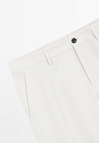 Pantaloni grigi chiari realizzati in un tessuto a trama liscia. Presentano una chiusura con bottone, passanti per cintura e tasche laterali. Design pulito e su misura.