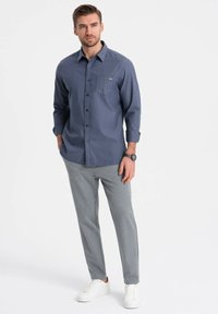 Lichtblauw button-up shirt met een borstzak, gecombineerd met lichtgrijze slim-fit broek en witte sneakers. Soepele stof, casual ontwerp.