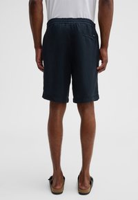 Pantaloni corti di cotone blu navy con vita regolabile, tasche laterali, orli ripiegati e una tasca posteriore singola. Texture liscia e design informale.