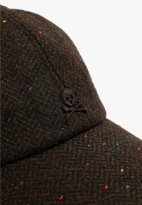 Gorra de lana marrón con un patrón de espiga, que presenta motas de colores. Detalle bordado de calavera y tibias cruzadas en la parte delantera.