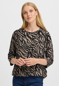 Beige topp med ett mönster av svarta zebraränder, avslappnad passform, rund halsringning och 3/4 ärmar. Tyget ser mjukt och lättviktigt ut.